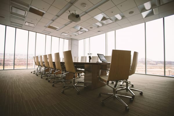 Empty conference room with a long table, wooden chairs, and floor-to-ceiling windows allowing natural light.