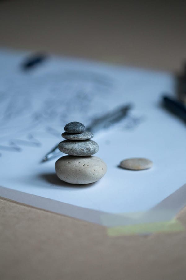 A small stack of smooth stones is placed on a piece of paper, with a pen and an additional stone nearby.