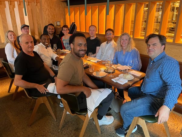 A group of people sitting around a table in a restaurant, smiling and looking at the camera.